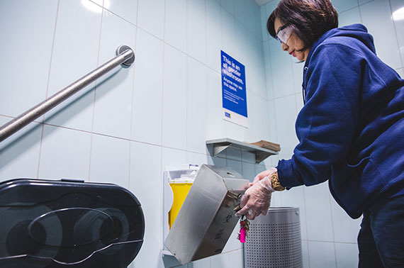 A member of the Facilities Management and Development team safely chaining the sharps disposal container in a washroom. 
