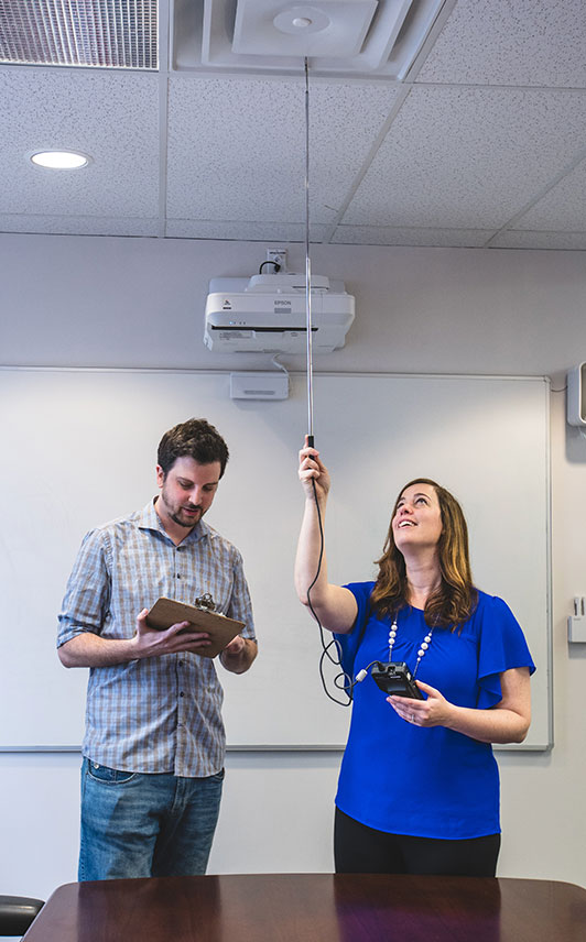 A member of the Environmental Health and Safety team checking the air velocity in a meeting room with a departmental safety officer. 