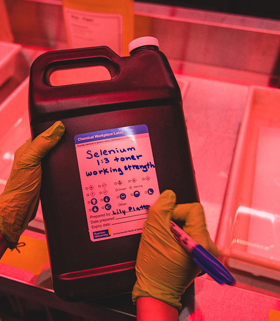 A person in a darkroom filling out a chemical label.
