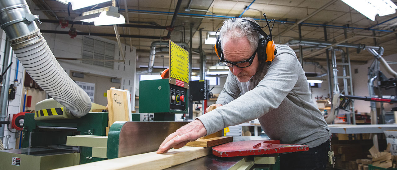 A person working at a large table saw while wearing ear protection. 