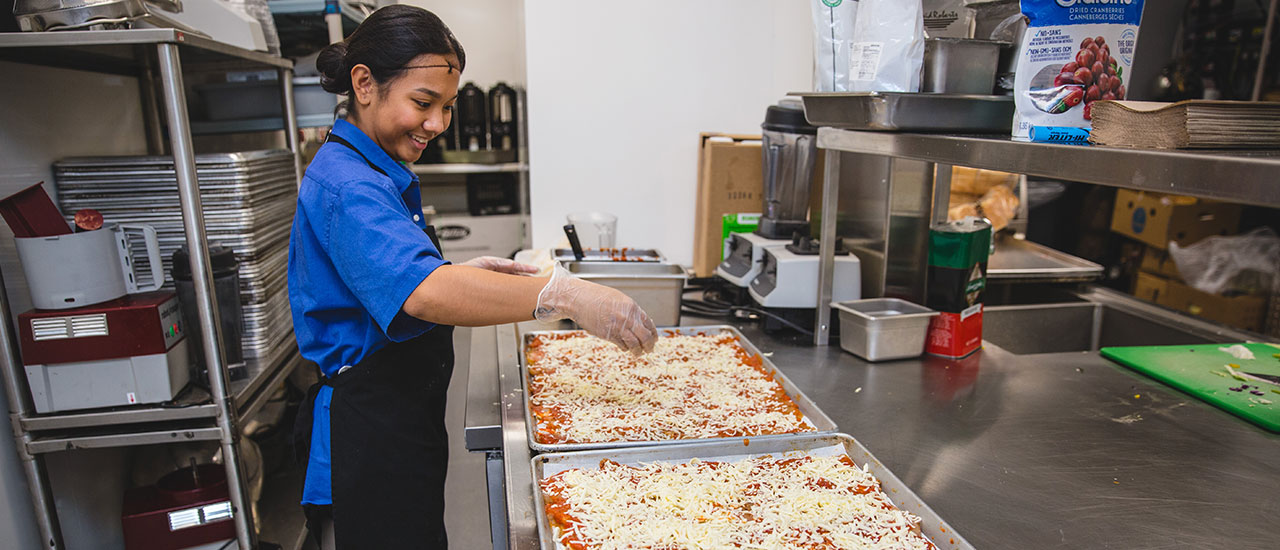 A chef from food services preparing the toppings on two large pizzas.