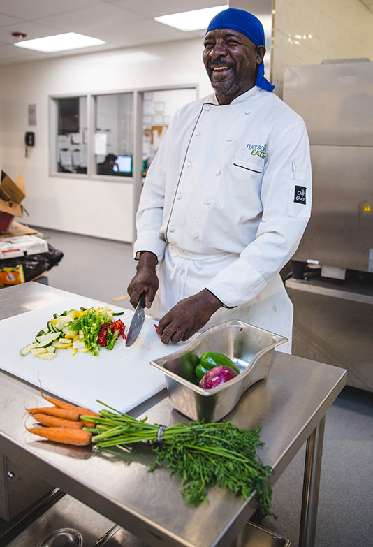 A chef from food services smiling while chopping fresh vegetables.