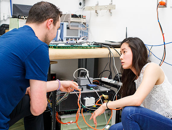 Two students looking at wires on a piece of electrical equipment. 
