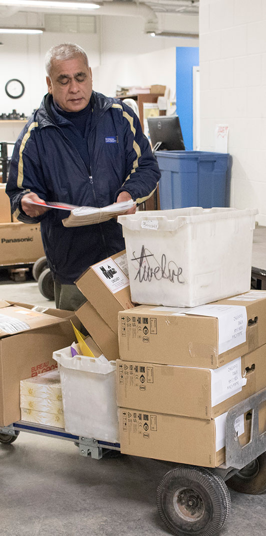 A staff member in the mailroom loading a trolly with boxes for delivery.