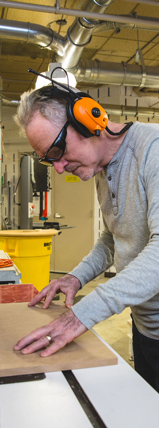 A person working at a large table saw while wearing ear protection. 