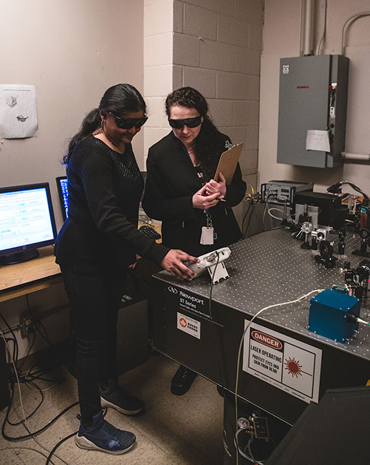 A member of the Environmental Health and Safety team reviewing laser lab equipment with a departmental safety officer.