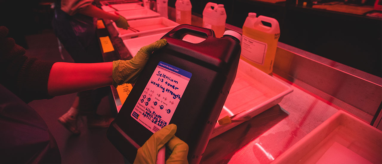 A person in a darkroom filling out a chemical label. 