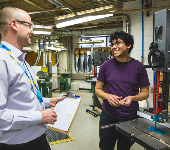 A member of the Environmental Health and Safety team smiling and chatting with an architecture student in a workshop. 