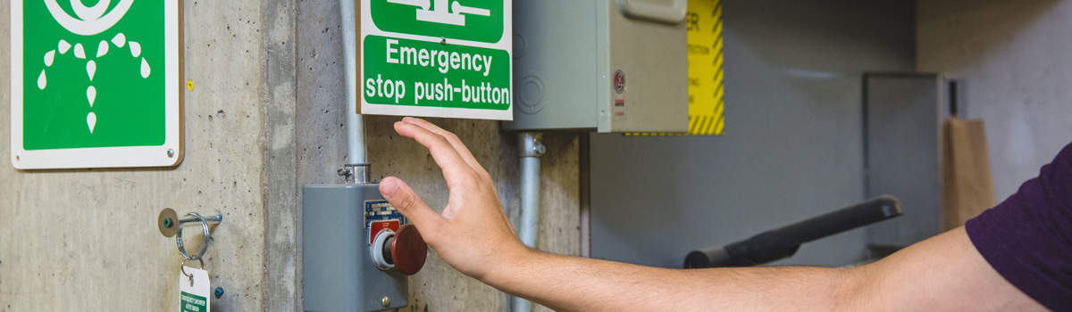 A hand reaching for the emergency stop button in a workshop.