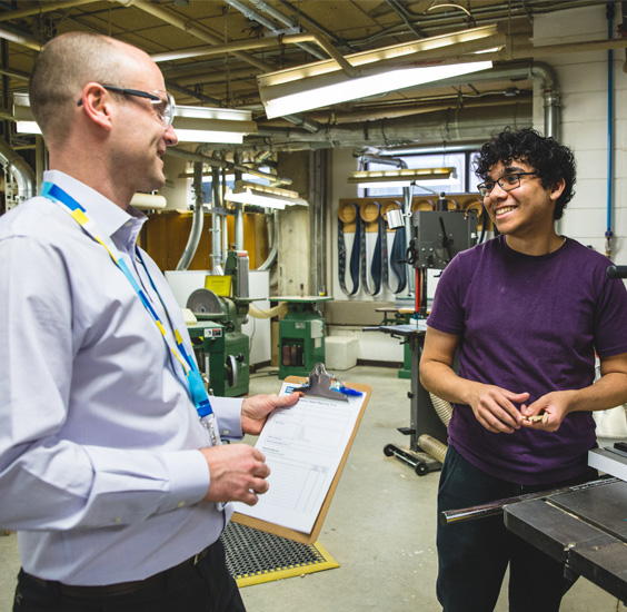 A member of the Environmental Health and Safety team smiling and chatting with an architecture student in a workshop.