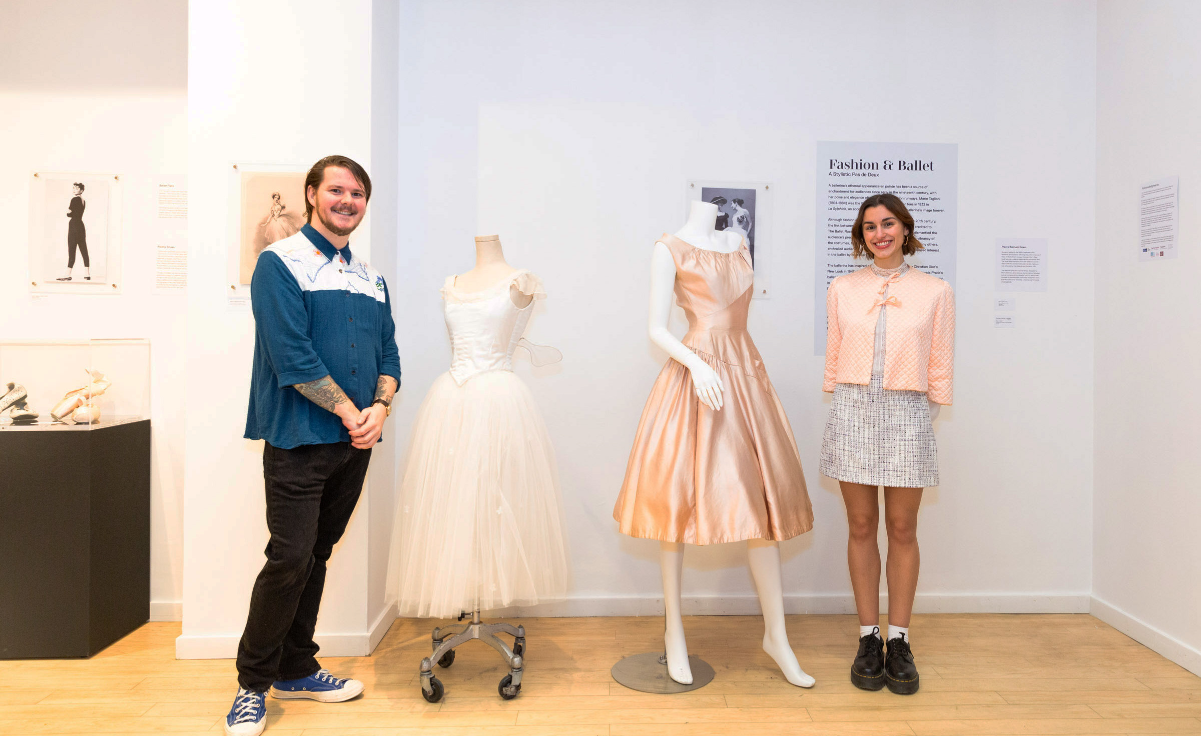 Patrick Taylor and Sofia Beraldo standing next to two dresses, one white and one pink. 