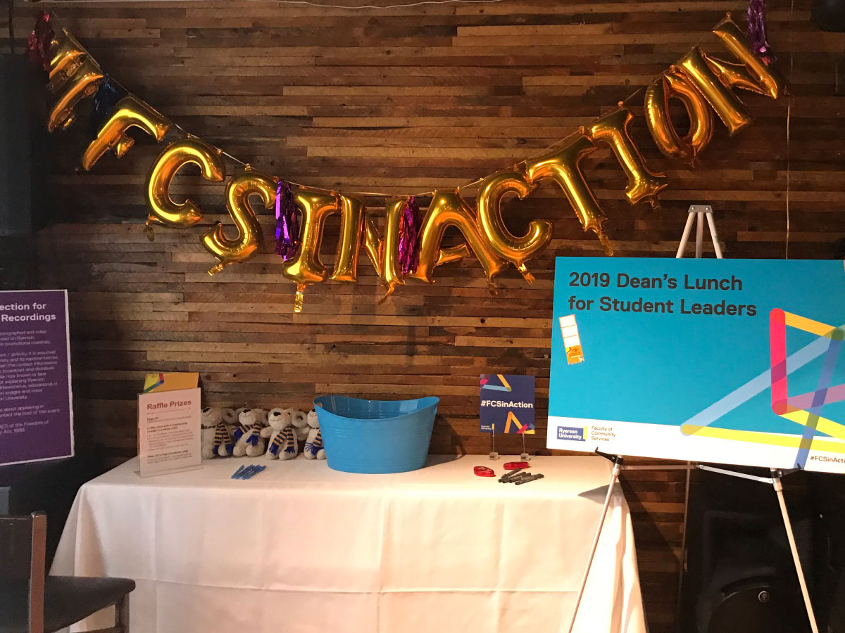 Metallic balloons reading 'FCS in action' , hanging over table of raffle prizes.