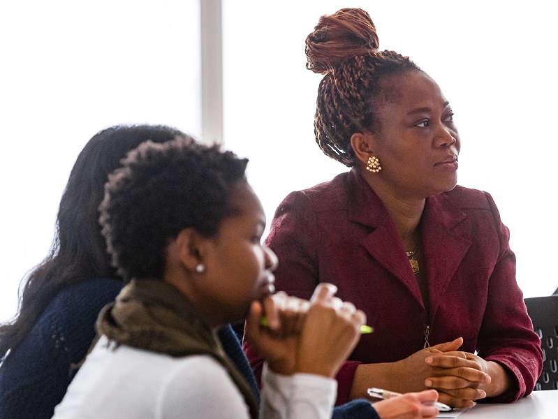 Three women sit around a table in a classroom setting