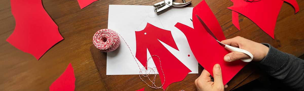 Someone cutting the shape of a little red dress out of frabric material as an activity that honours missing and murdered Indigenous Women