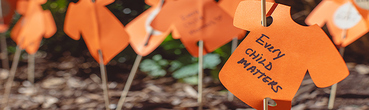 A small t-shirt cut out in orange paper, with the writing “every child matters”.