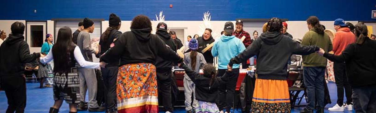 Community members holding hands in a circle around a group of singers and drummers at the round dance