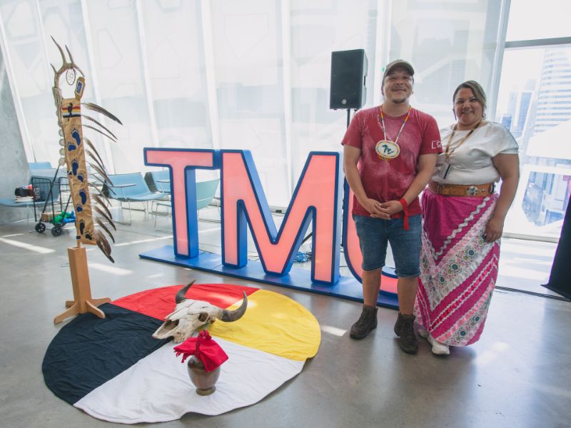  Waasekom and Crystal Osawamick stand in front of the TMU letter with the TMU eagle staff, buffalo skull and medicine wheel blanket.