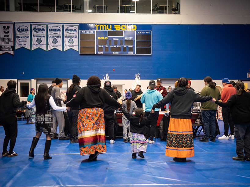 Community members holding hands in a circle around a group of singers and drummers at the round dance