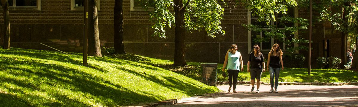 Three people walk side-by-side through the TMU quad on a sunny summer day