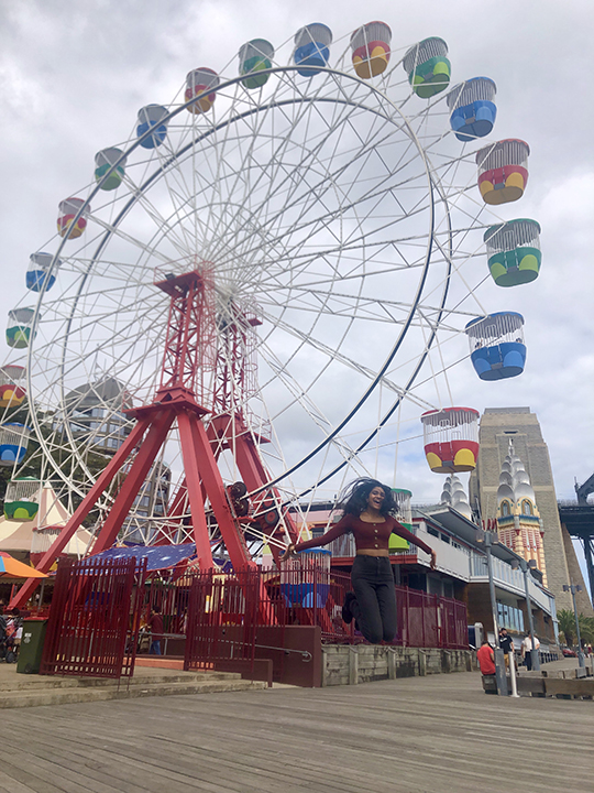 Sidra Jafri jumping in front of a Ferris Wheel.