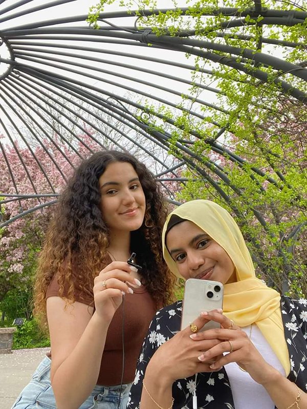 Third-year students Sania Ali and Dana Masamra posing with a microphone and phone as if they are going to start recording.