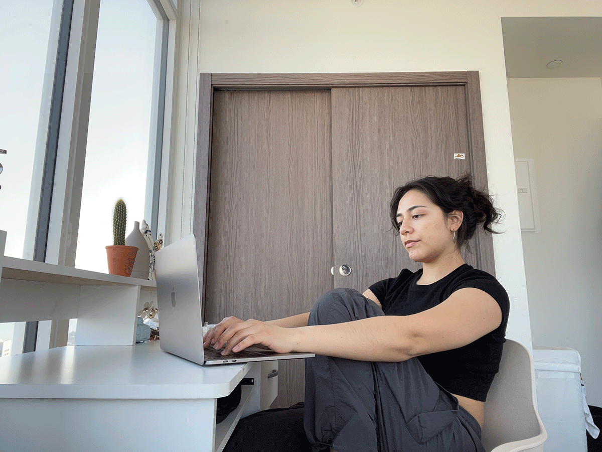 Manuela Vega sitting at her desk in her apartment working on her laptop.