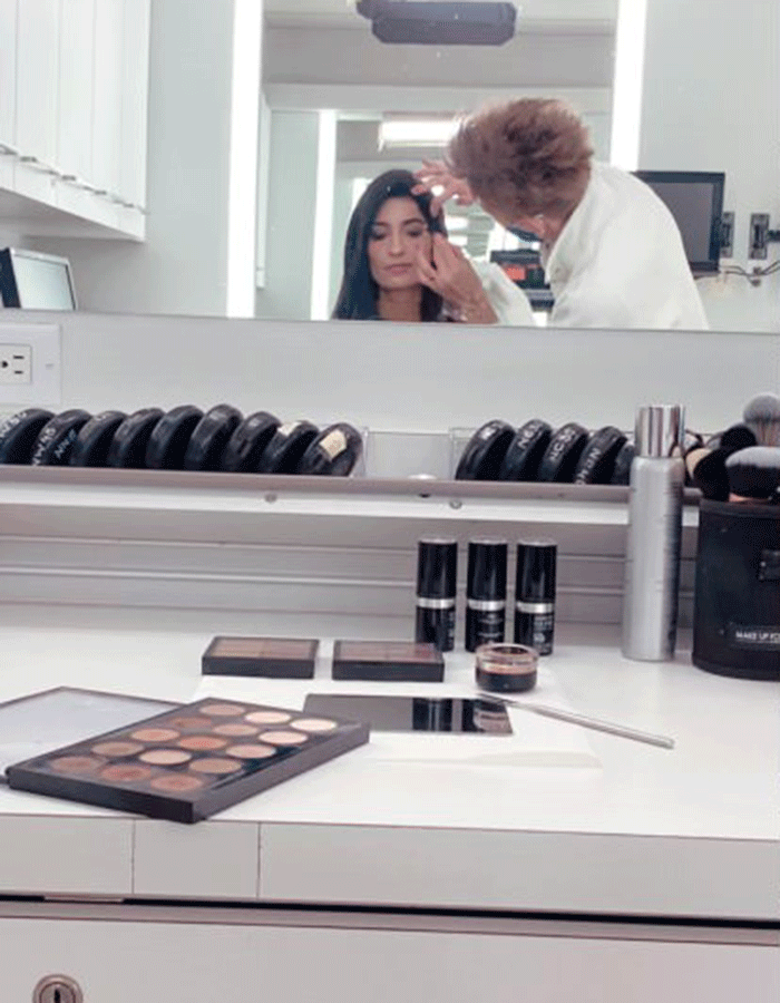 Leena Latafat's reflection in the mirror of the makeup counter while an artist applies her makeup