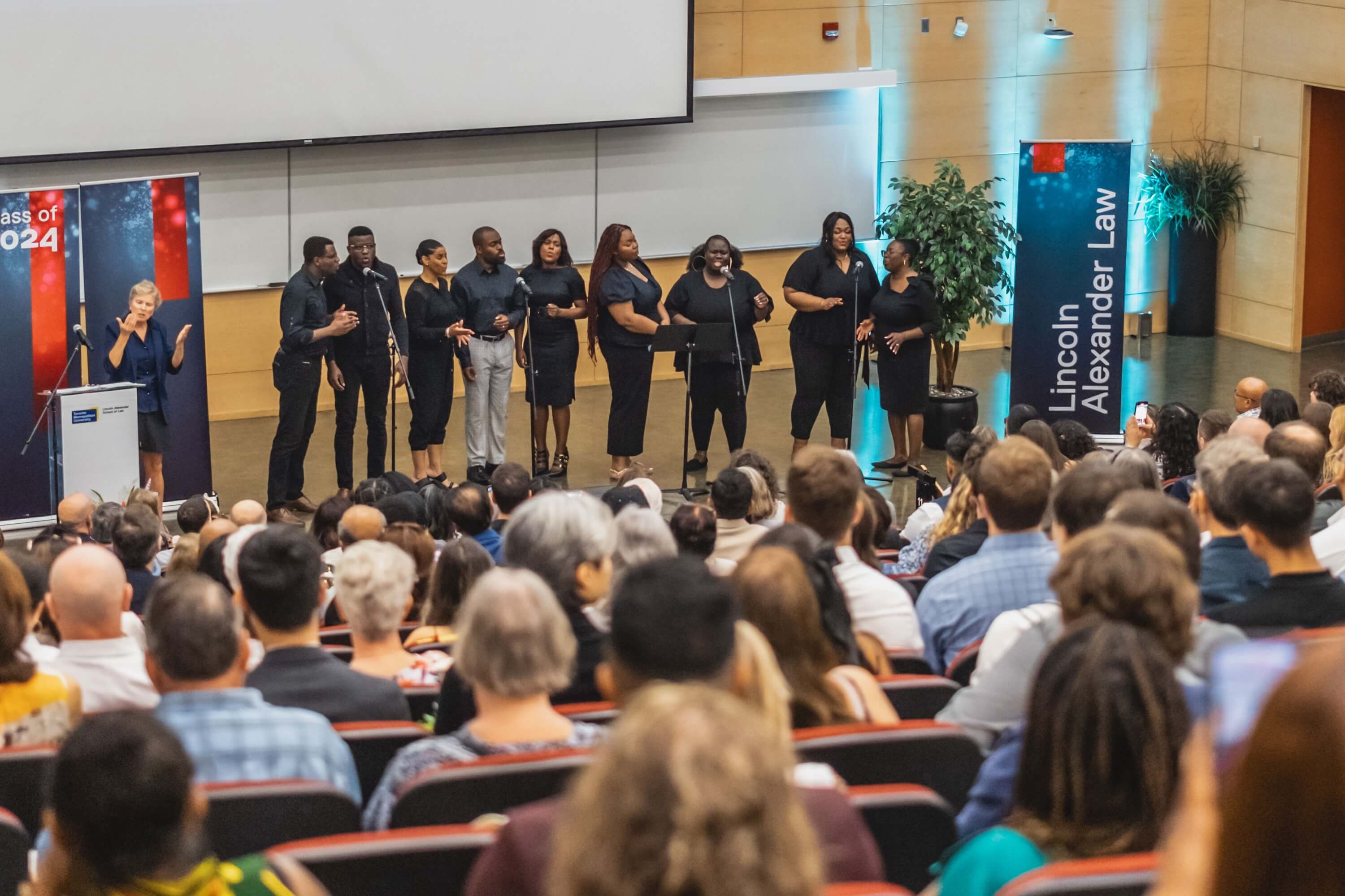 A group of singers all wearing black clothes performing for an audience in an auditorium. 