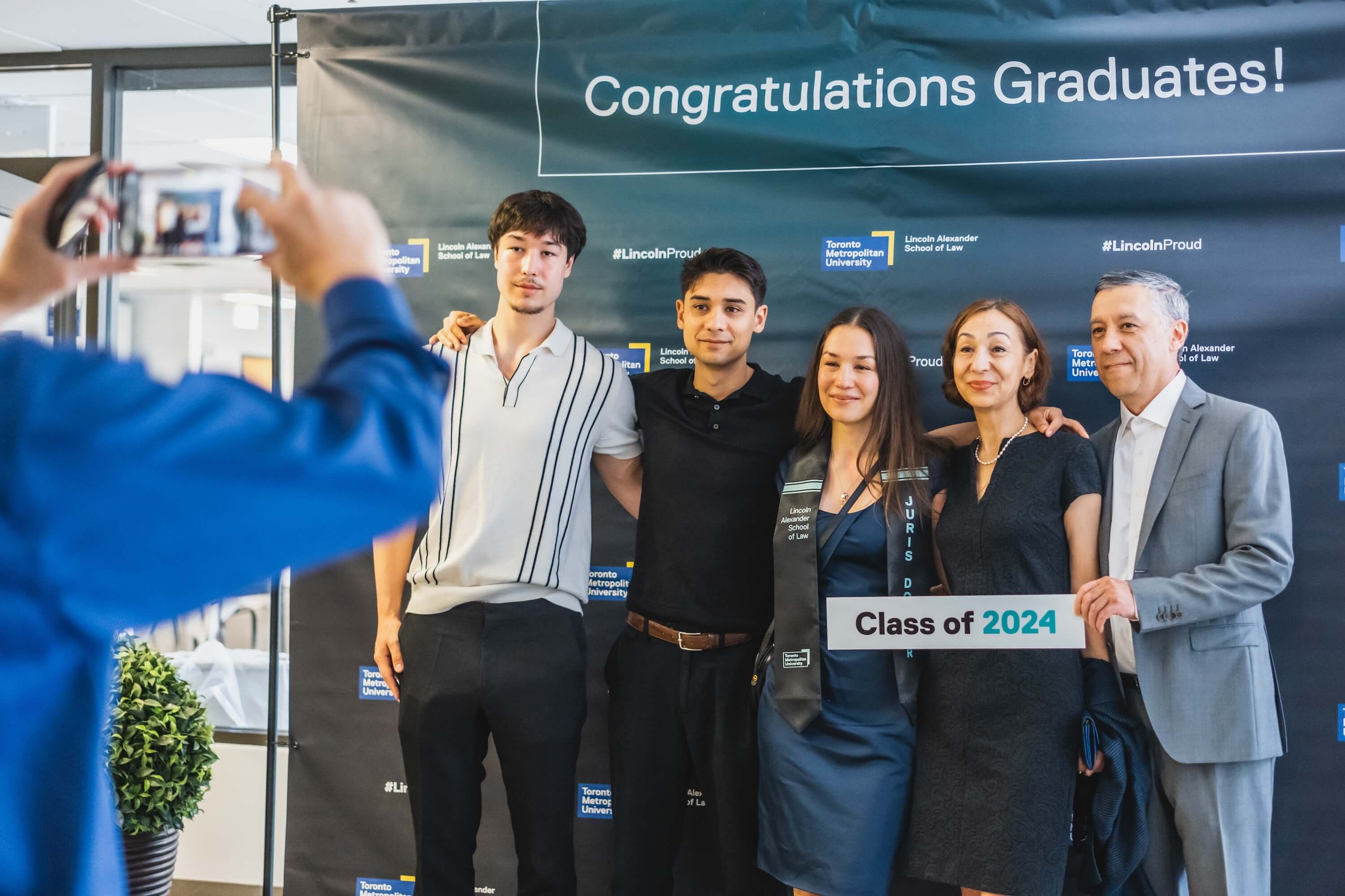 A small group of people standing in front of a "Congratulations Graduates!" banner having their photo taken.