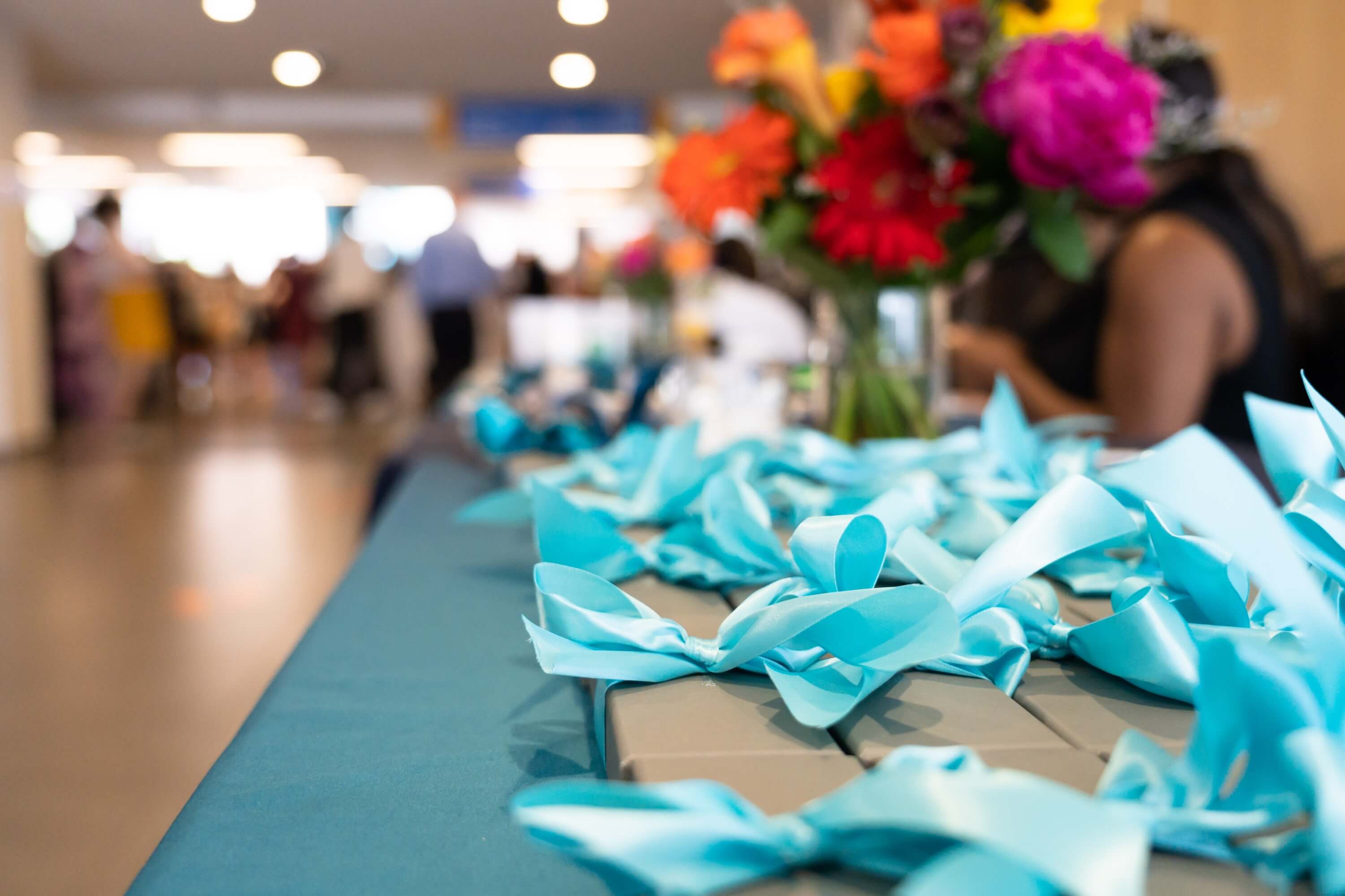 Gray boxes tied with a blue ribbon on a table with flowers in the background.