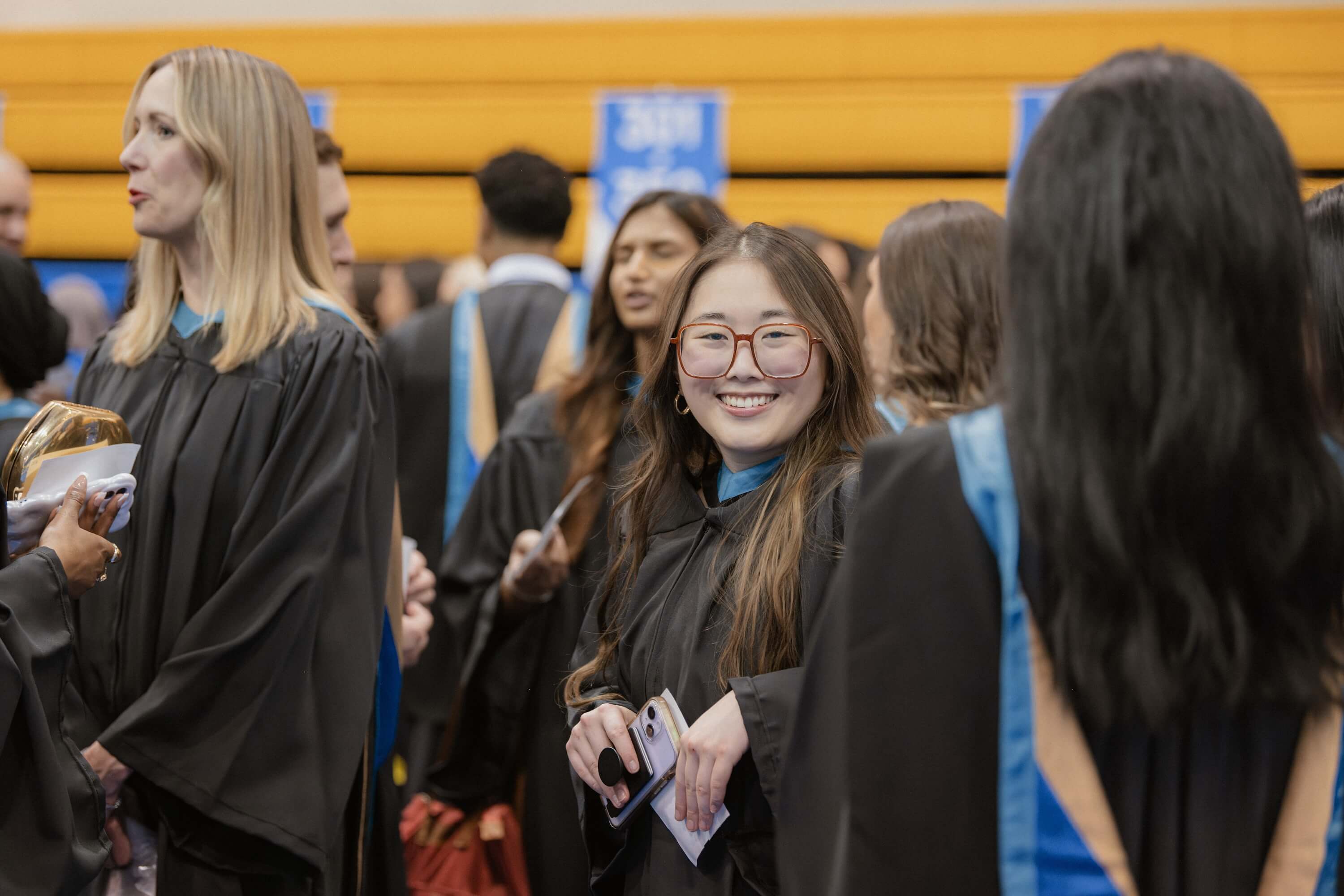 A woman smiling at the camera, surrounded by fellow graduates in graduation gowns at Convocation.