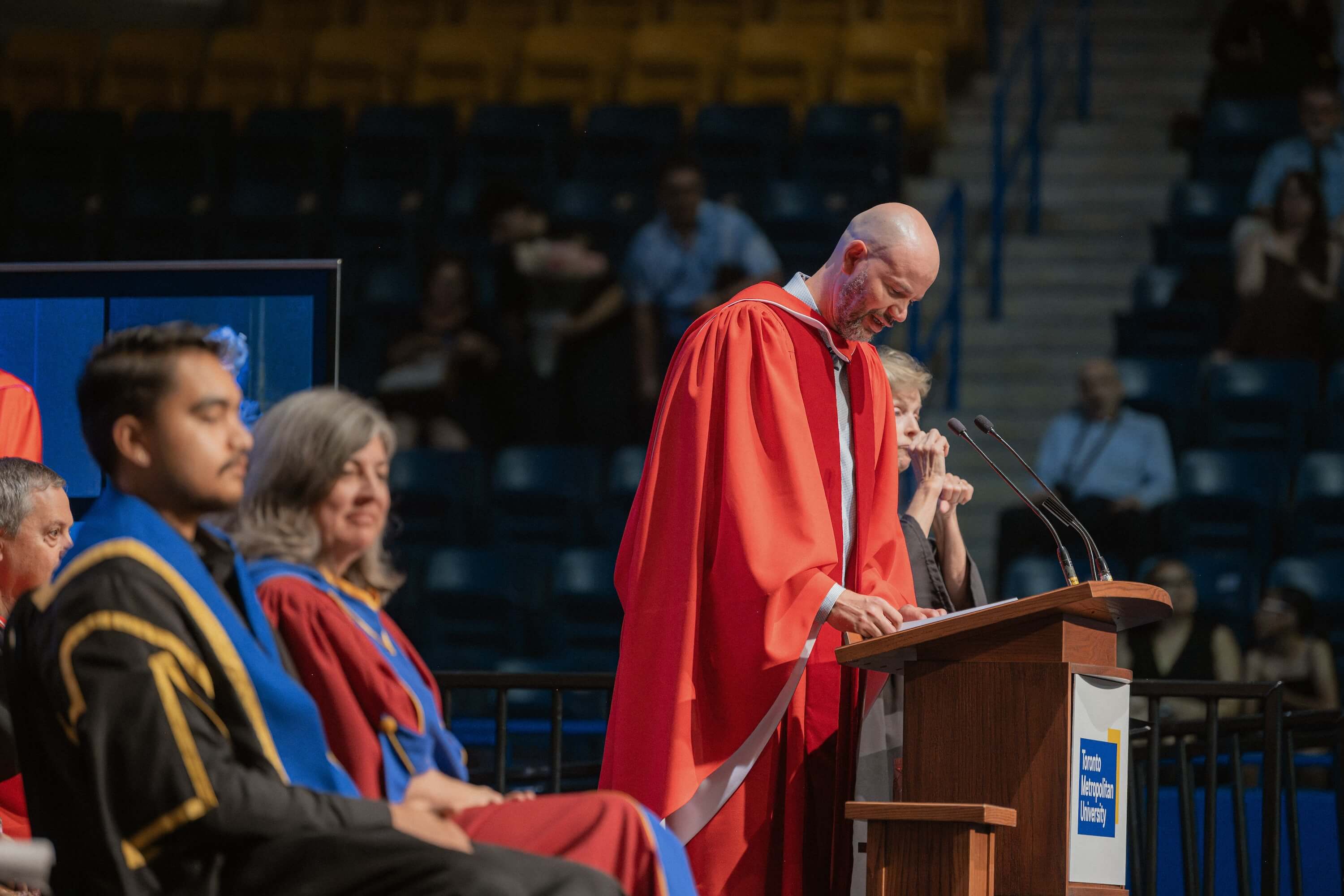 Dean Graham Hudson speaking from a podium on the stage at Convocation.