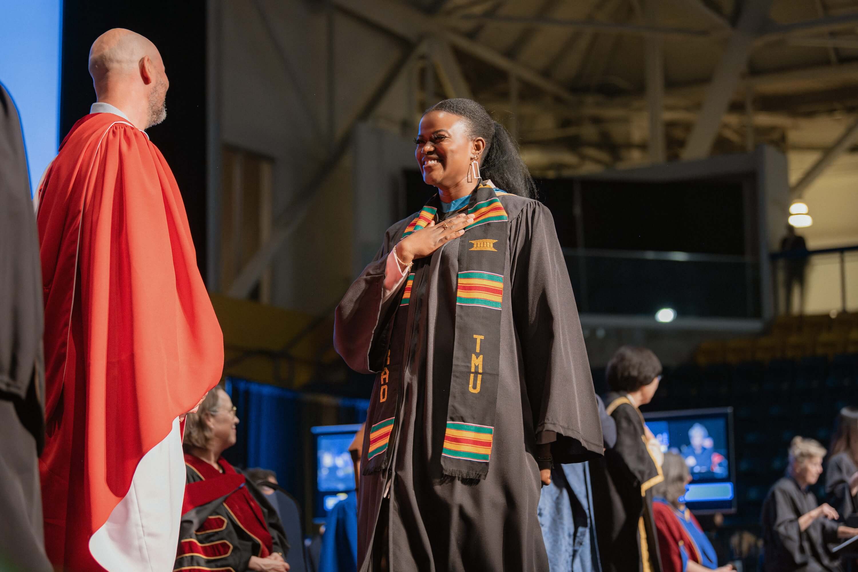 A woman walking across the stage toward Dean Graham Hudson at Convocation with her hand over her heart.