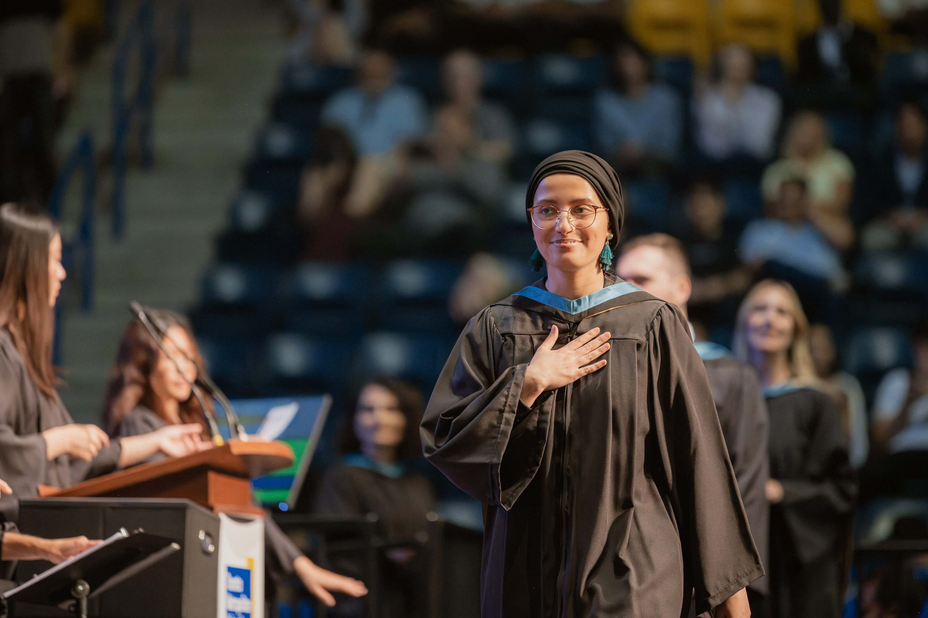 A woman with her hand on her heart walking across the stage at Convocation.
