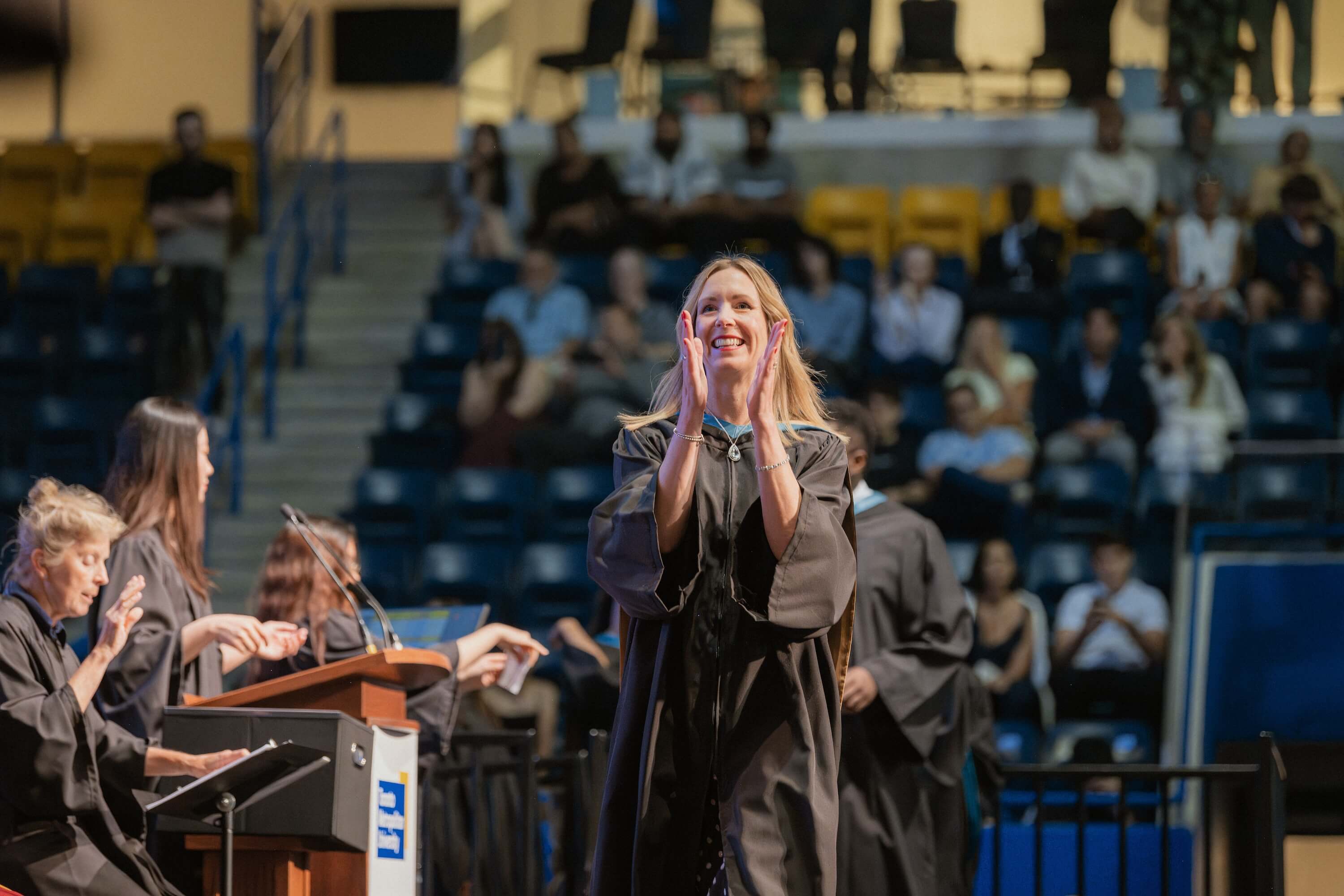 A woman clapping as she walks across a stage at Convocation.