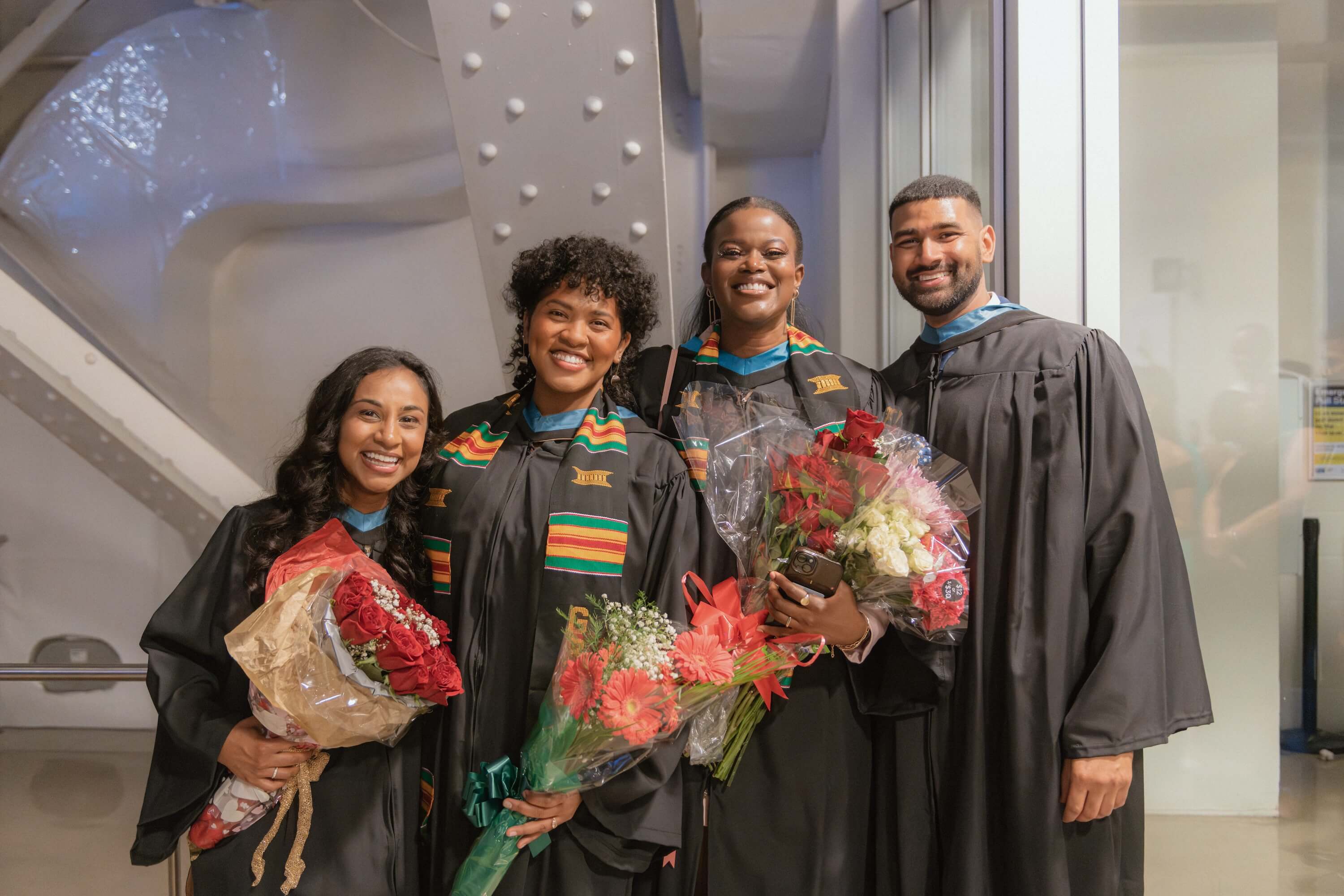 Four graduates pose with bouquets of flowers at Convocation.