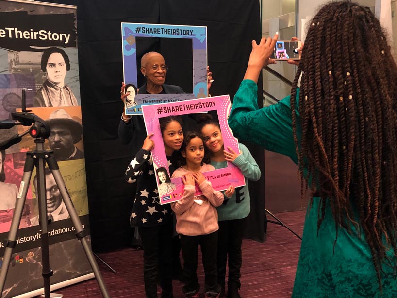 Multigenerational women hold cardboard cutouts while another woman takes a photo