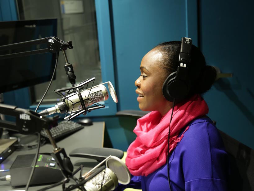 A Black woman in a recording studio speaking into a mic