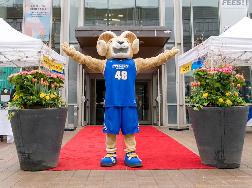 Eggy the Ram standing in between two planters with his arms outstretched