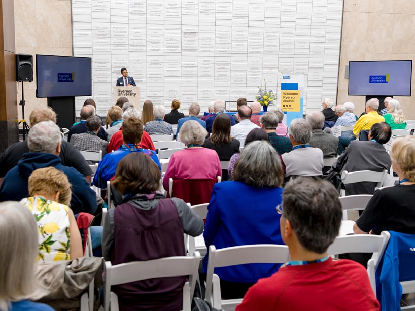 Krishan Mehta talking at a podium, facing a crowd of seated people