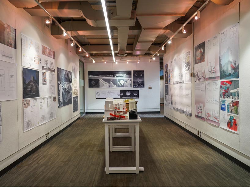 Wide angle shot of room with table in centre with architecture models on it and drawings on walls