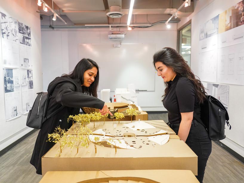 Two women pointing and looking at a mini model of an outdoor space