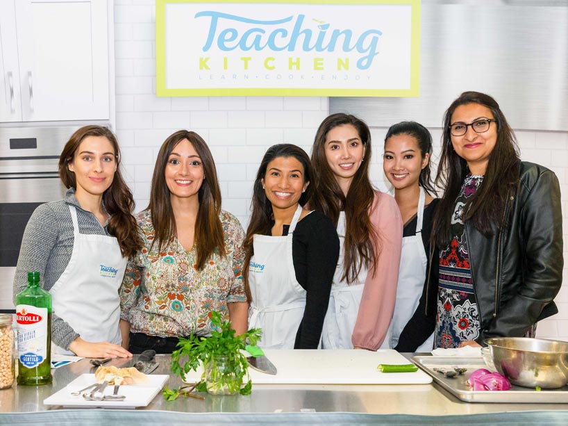 Six smiling women, standing behind a kitchen counter