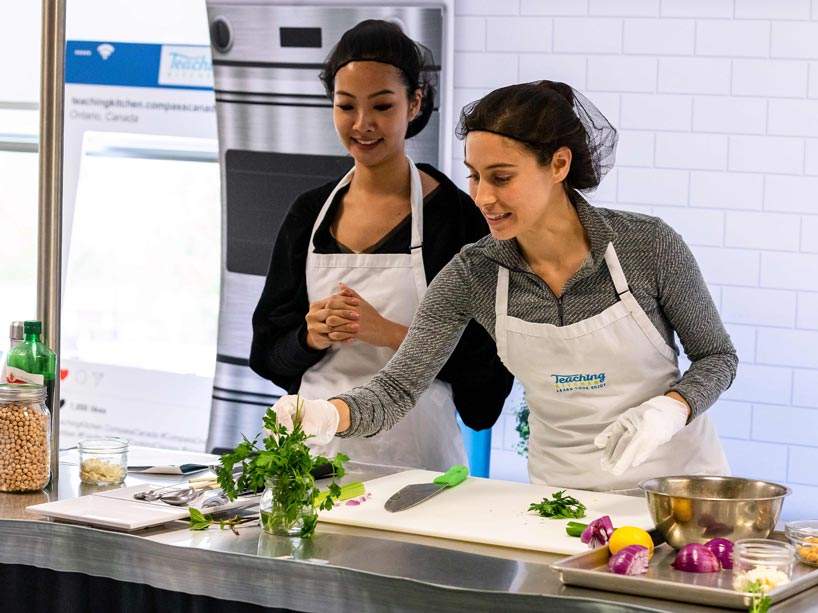 One woman picking herbs from a jar while another woman watches