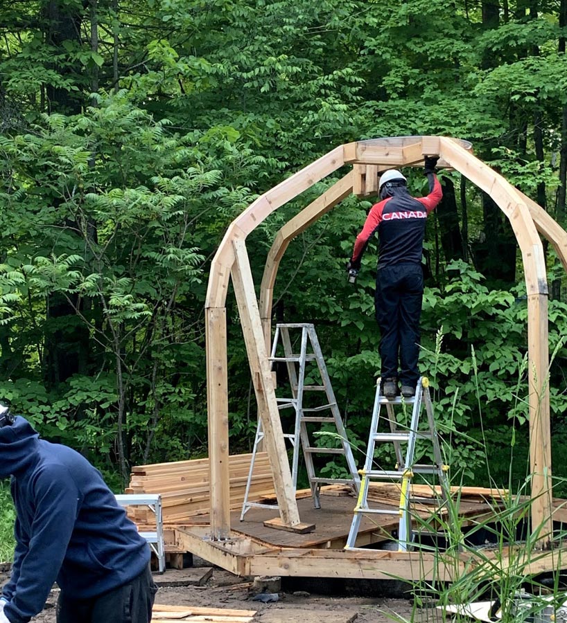 A student standing on a ladder building the wooden structure