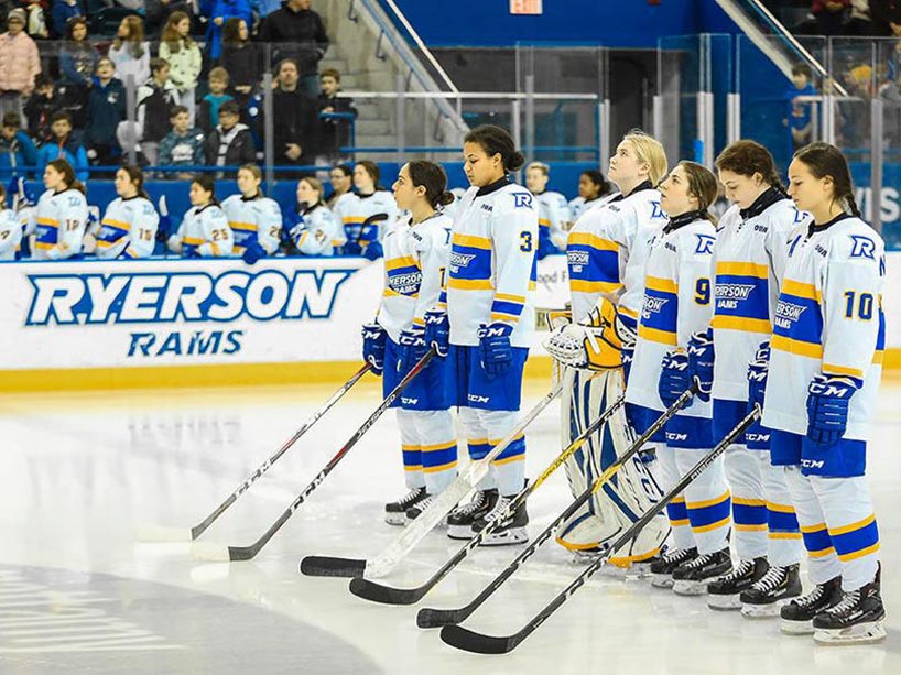 Female hockey players lined up shoulder to shoulder on the ice 