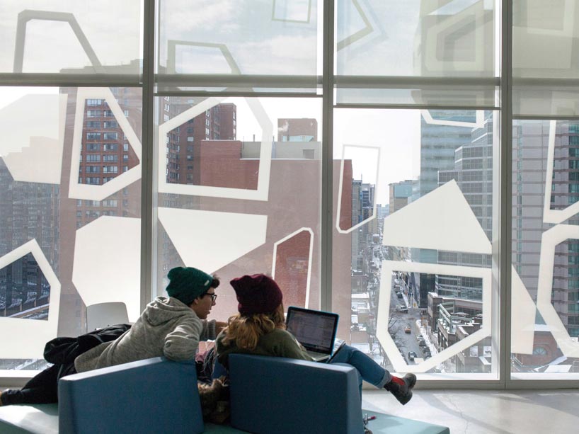 Two students sitting in chairs, working on a laptop, facing the window