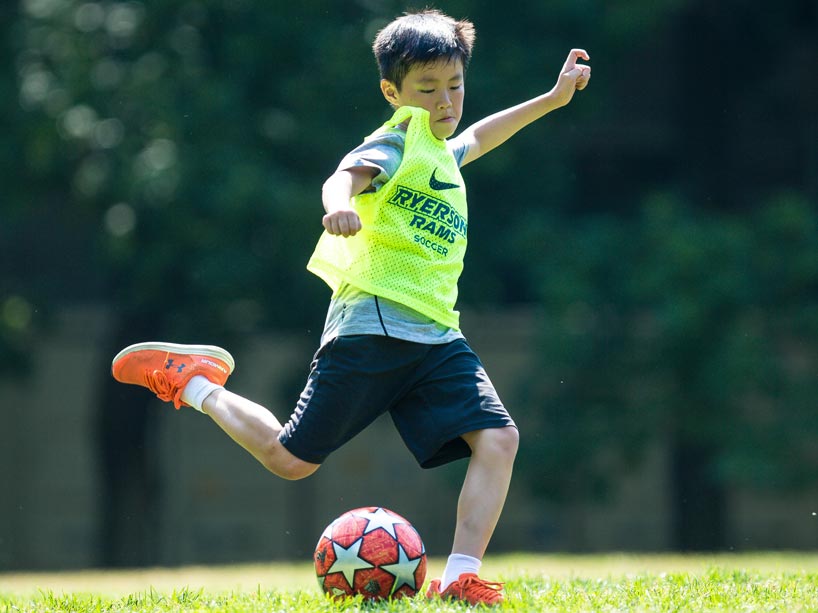 A boy wearing a Ryerson Rams jersey kicks a soccer ball