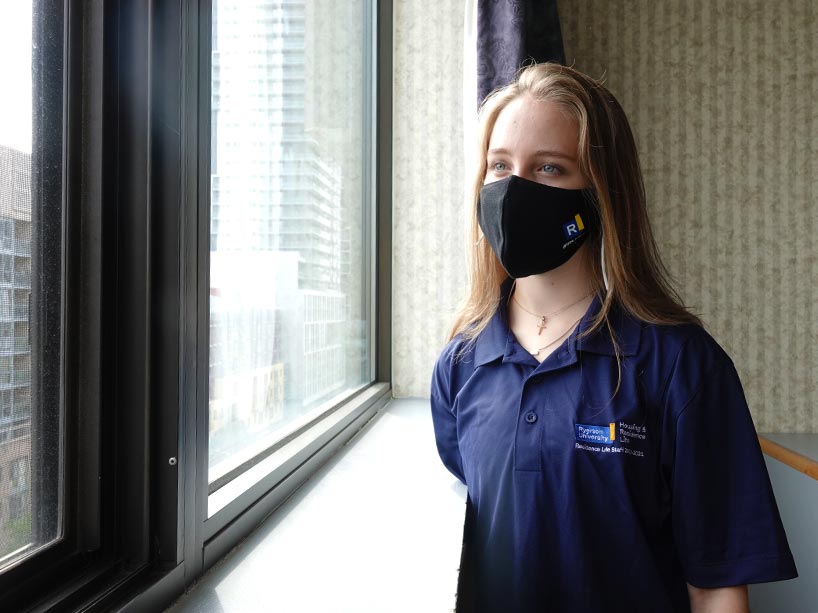 A student wearing a mask standing beside a window