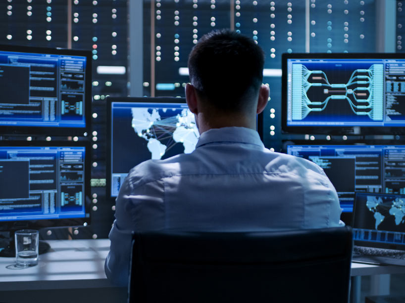 A man sits in front of several computers displaying a variety of information 